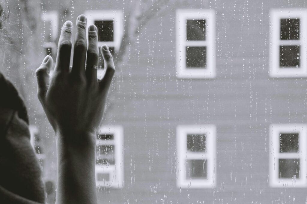 hand touching the glass window during rainy day