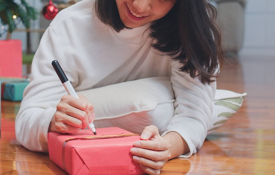 Image of a smiling teen girl writing on a wrapped Christmas present. Help your teen heal from their past trauma with the help of trauma therapy in South Jersey to begin coping and healing from their symptoms. 