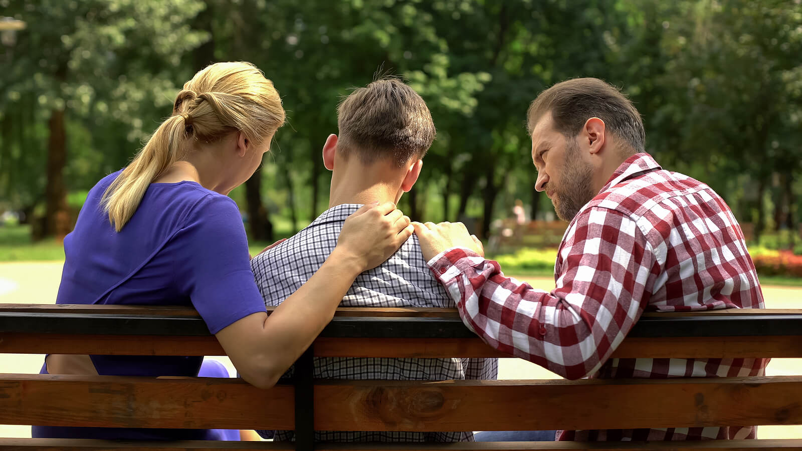 Image of supportive parents sitting on a bench comforting their teen boy. If your teen struggles with trauma during the holiday season, trauma therapy in South Jersey can help them develop healthy coping strategies to begin healing.