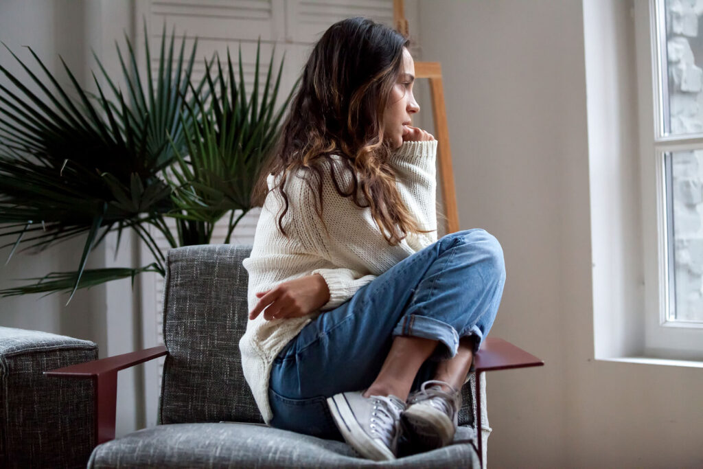 Image of a young teen girl sitting in a chair looking out a window. Begin supporting your teen and help them manage past trauma during the holidays with the help of trauma therapy in South Jersey.