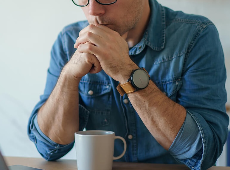 Image of a thoughtful man sitting at a table resting his chin on his hands. With the help of trauma therapy in South Jersey you can begin working on creating healthy boundaries with family.