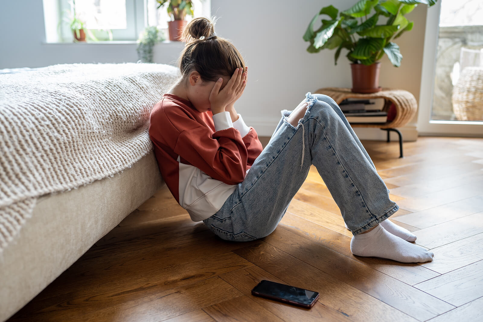 Image of an upset teen girl sitting on the floor covering her face. Support your teen in healing from past trauma during the holidays with the help of a skilled trauma therapist in South Jersey.