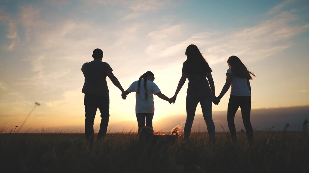 Image of a happy family holding hands while walking through a field holding hands. With the help of therapy for children and teens in South Jersey your child can begin working on emotional regulation.