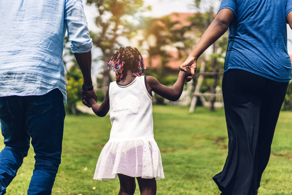 Image of two parents holding a young girls hands while walking through a park. Discover how you can better support your child managing their emotions with the help of DBT therapy for children and teens in South Jersey.