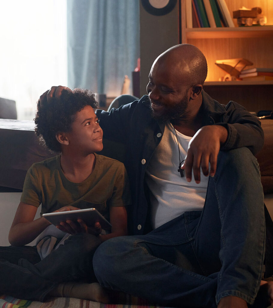 Image of a smiling father and son sitting in the floor looking at each other. Support your child with their overwhelming emotions with therapy for teens in South Jersey.