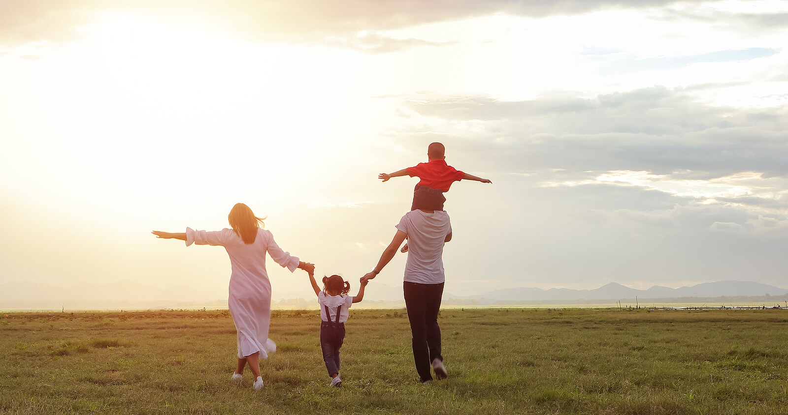 Image of a happy family walking through a field during sunset. If your child is struggling with big changes such as divorce, find support with the help of therapy for children in South Jersey.