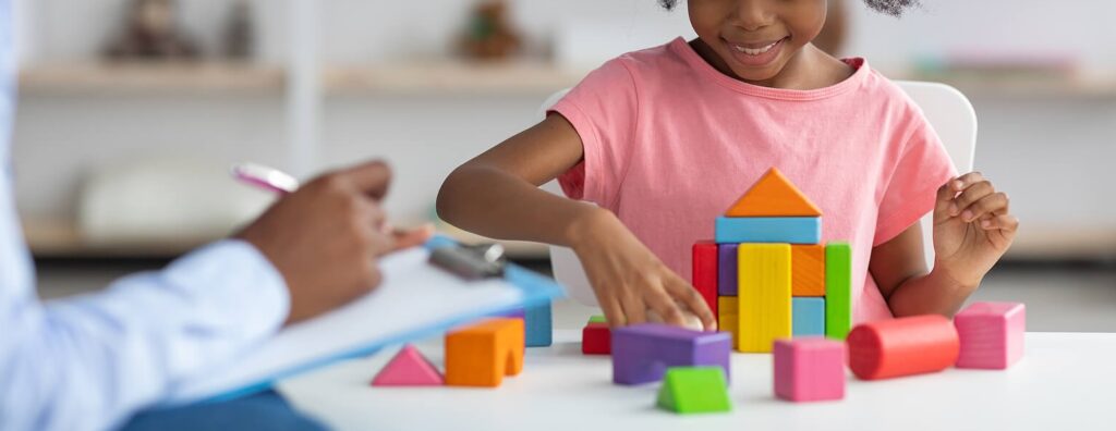 Image of a smiling little girl playing with blocks with a therapist. By working with a skilled child therapist in South Jersey, your child will begin coping with their unwanted emotions in positive ways.