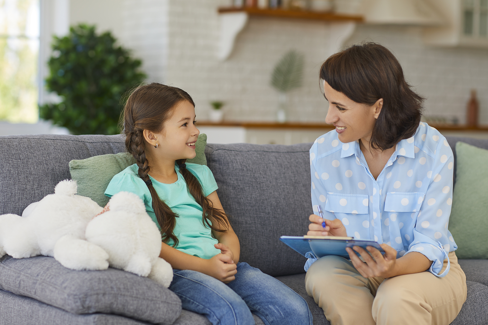 Happy little child talking with a therapist sitting on sofa during therapy session. With the help of a skilled child therapist in South Jersey, your child can begin to manage their emotions in positive ways.