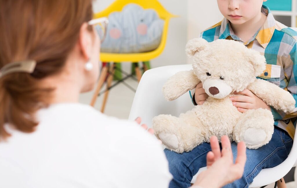 Image of a sad boy holding a stuffed bear while talking to a woman. If your child struggles to manage their big emotions, find support with therapy for children in South Jersey.