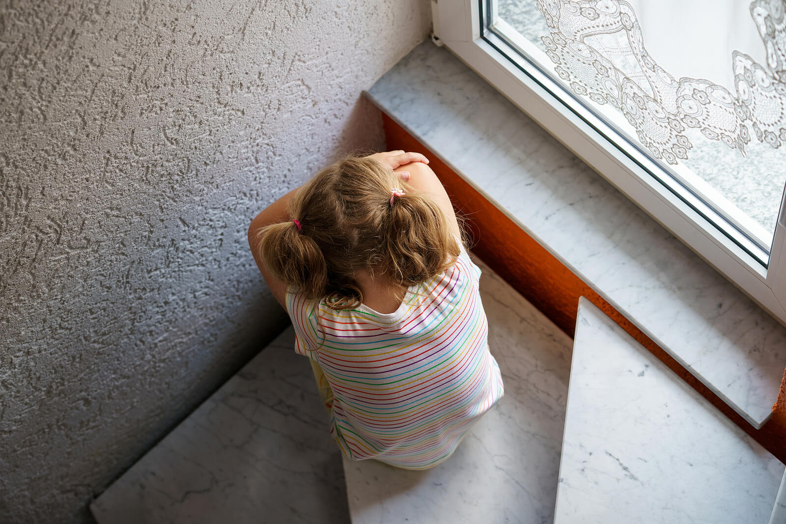 Image of a sad little girl sitting on a step with her head resting on her knees. If your child struggles with anxiety, find support with a skilled child therapist in South Jersey. Help them manage their symptoms soon.