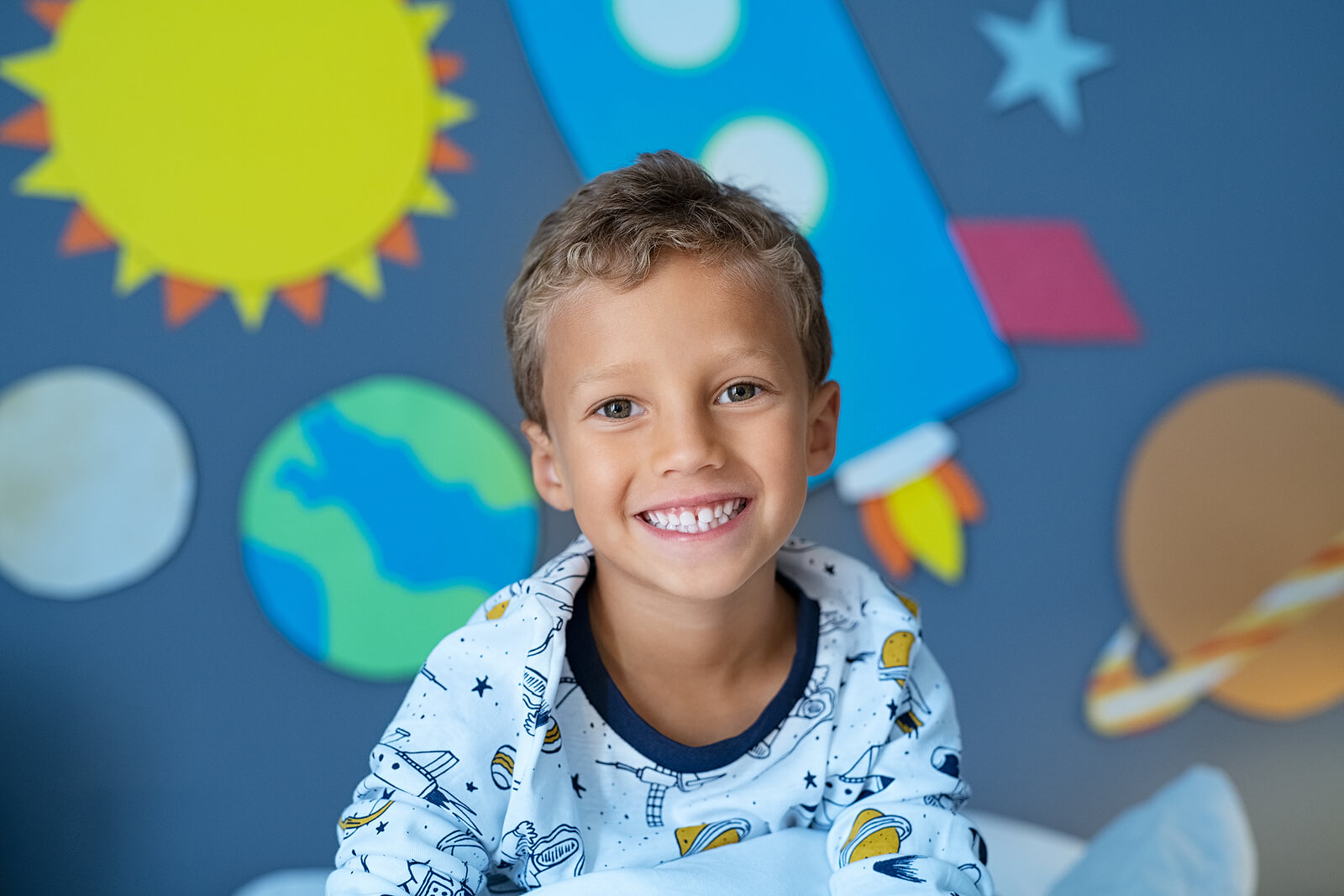 Image of a smiling boy sitting in space decorated bedroom with the solar system and planets made of cardboard attached to the wall. If your child struggles with their emotions and leads to unwanted behaviors, discover how therapy for children in South Jersey can help them begin coping.