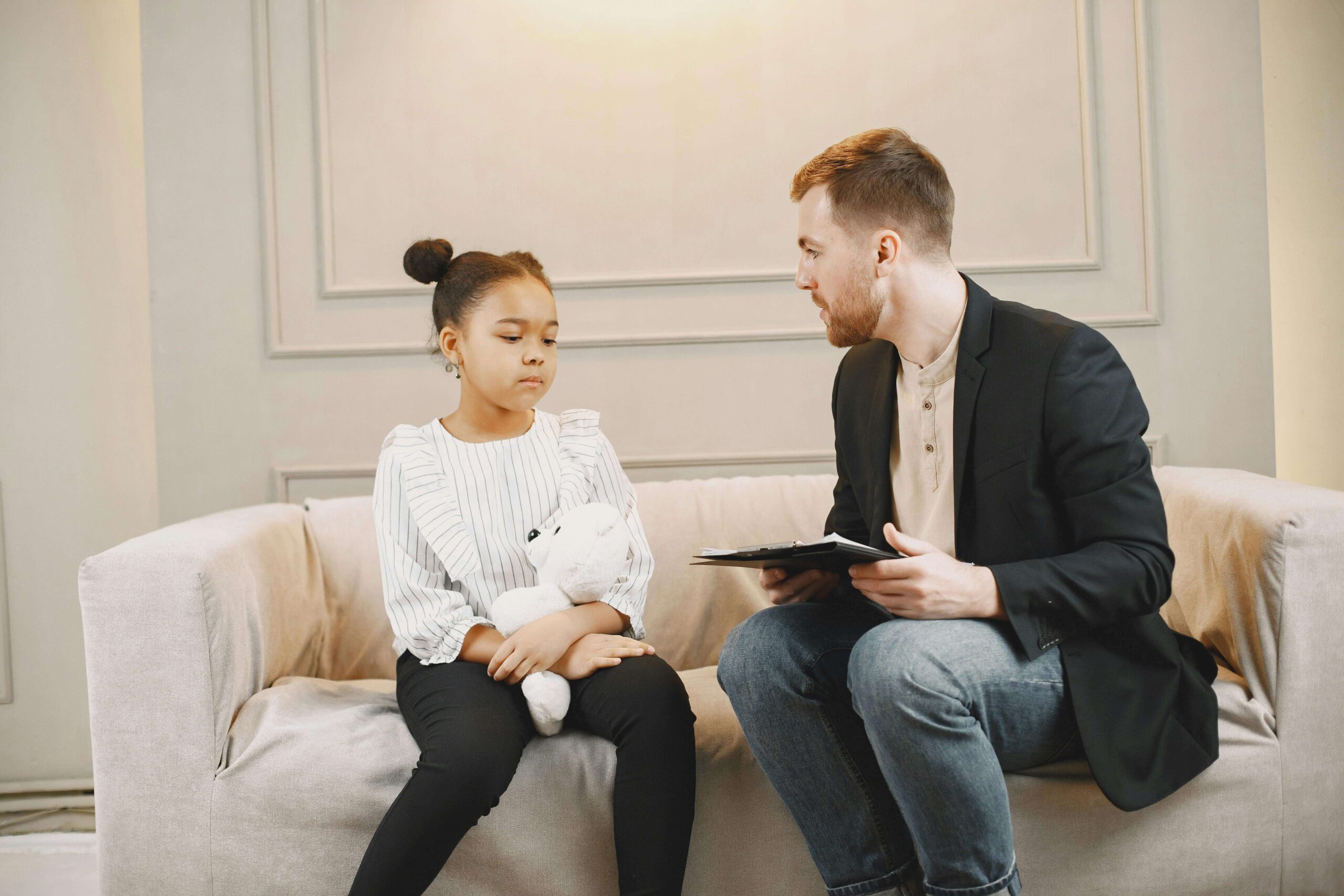 Image of a young girl sitting on a couch holding a teddy bear while listening to a child therapist. Therapy for children in South Jersey can help your child begin to overcome and thrive after struggling with anxiety.