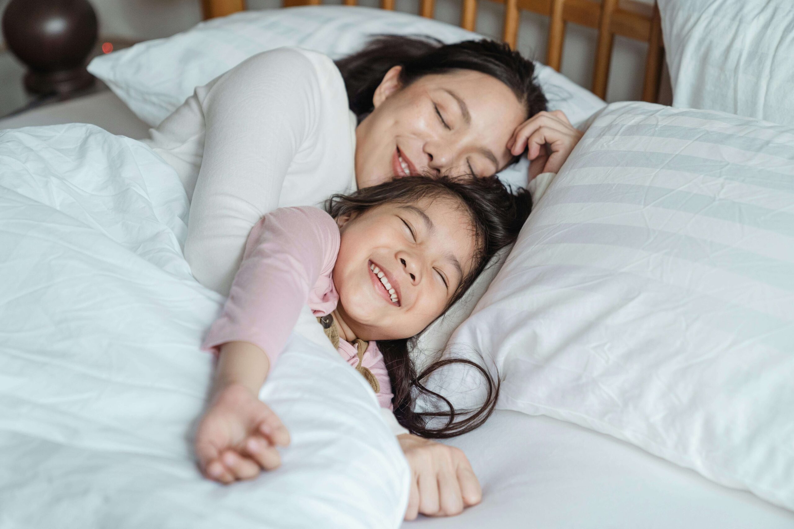 Image of an Asian American mom and daughter laying in bed snuggling and smiling. Therapy for children in South Jersey can help your child build emotional resilience and overcome their anxiety in positive ways. Find support soon!