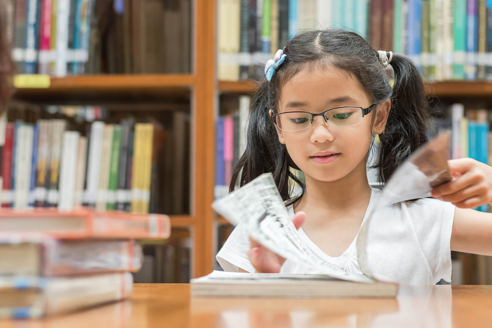 Smiling girl sitting in a library flipping through a book. With the help of a compassionate child therapist in South Jersey, you're child can begin to cope with their emotions and behaviors in positive ways.