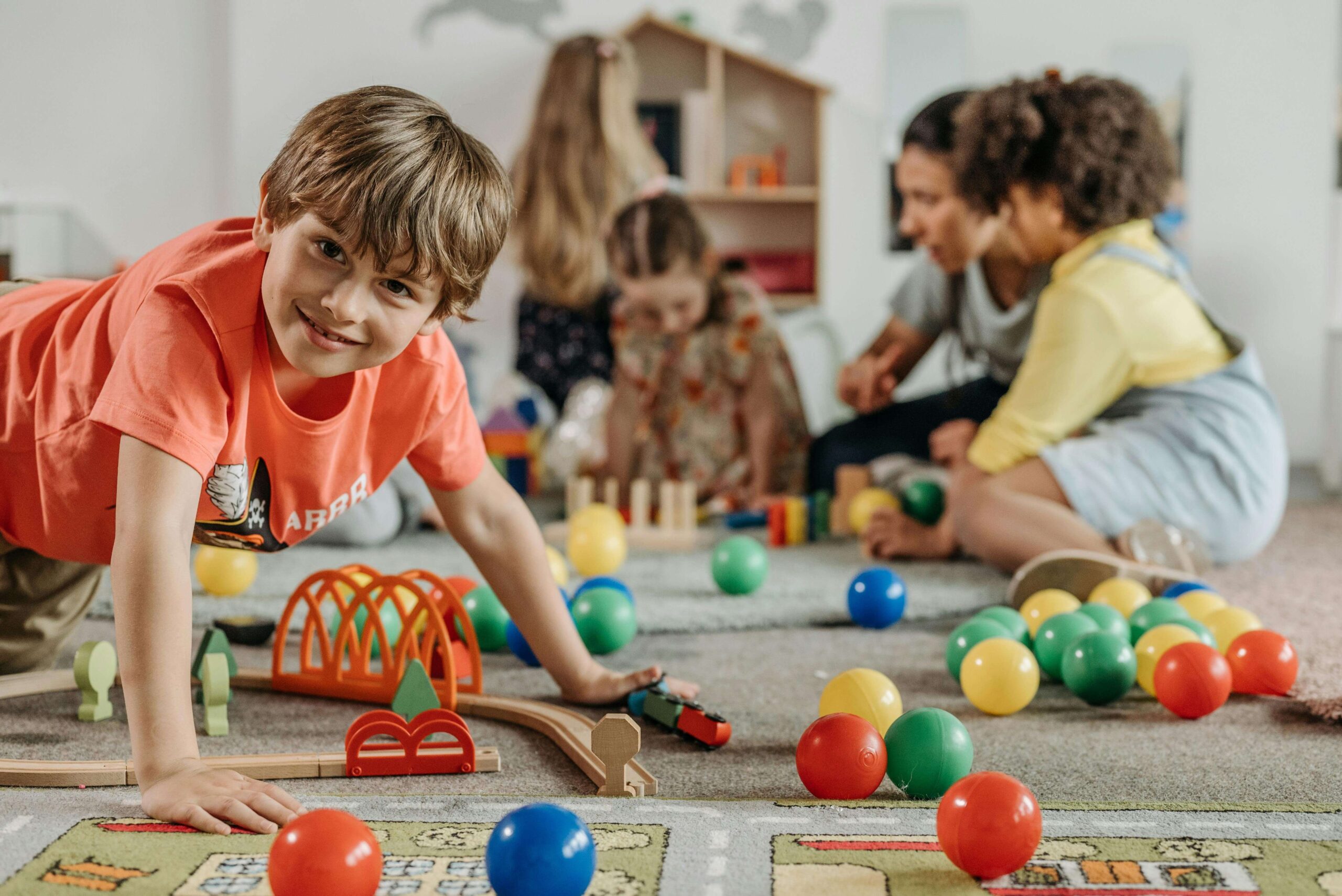Happy boy on the floor playing with toys with other children playing in the background. With therapy for children in South Jersey, your child can begin to build the confidence they need to heal from their anxiety symptoms. 