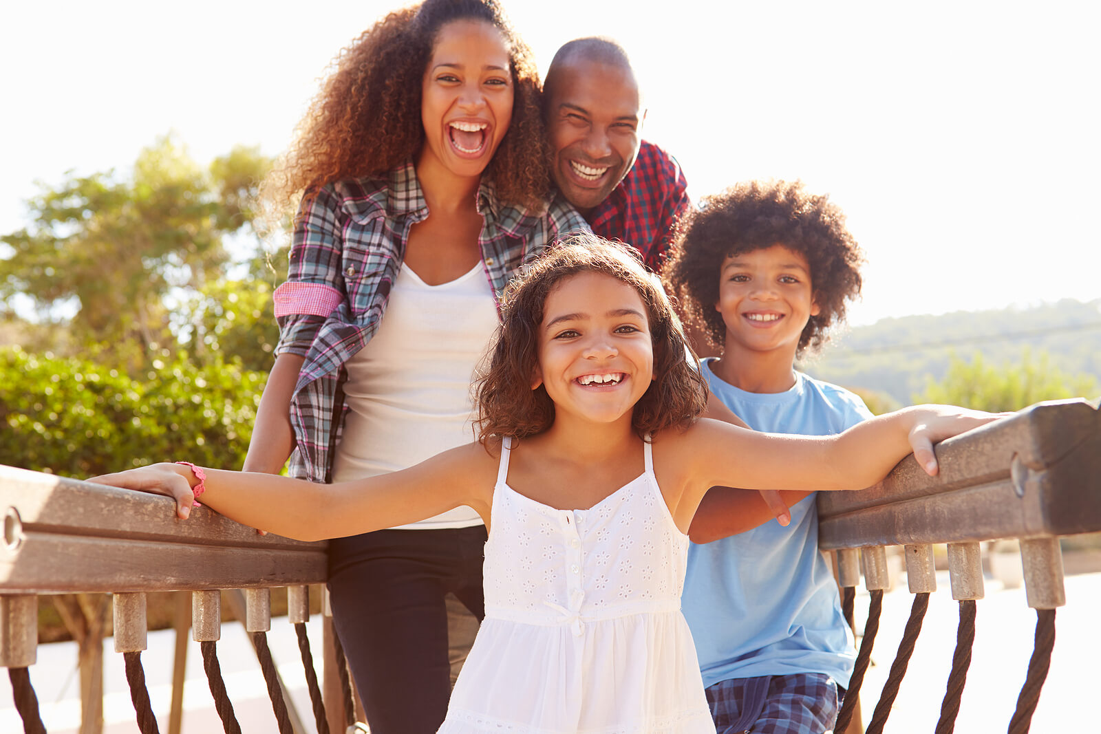 Happy family standing on a bridge laughing. See your child begin to express themselves in positive ways after learning to manage their emotions and behaviors with therapy for children in South Jersey.