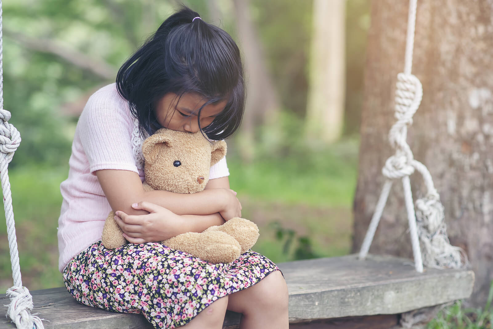 Sad little girl on a swing hugging a teddy bear. See your child begin to thrive as they learn to manage their emotions with the support of a child therapist in South Jersey.