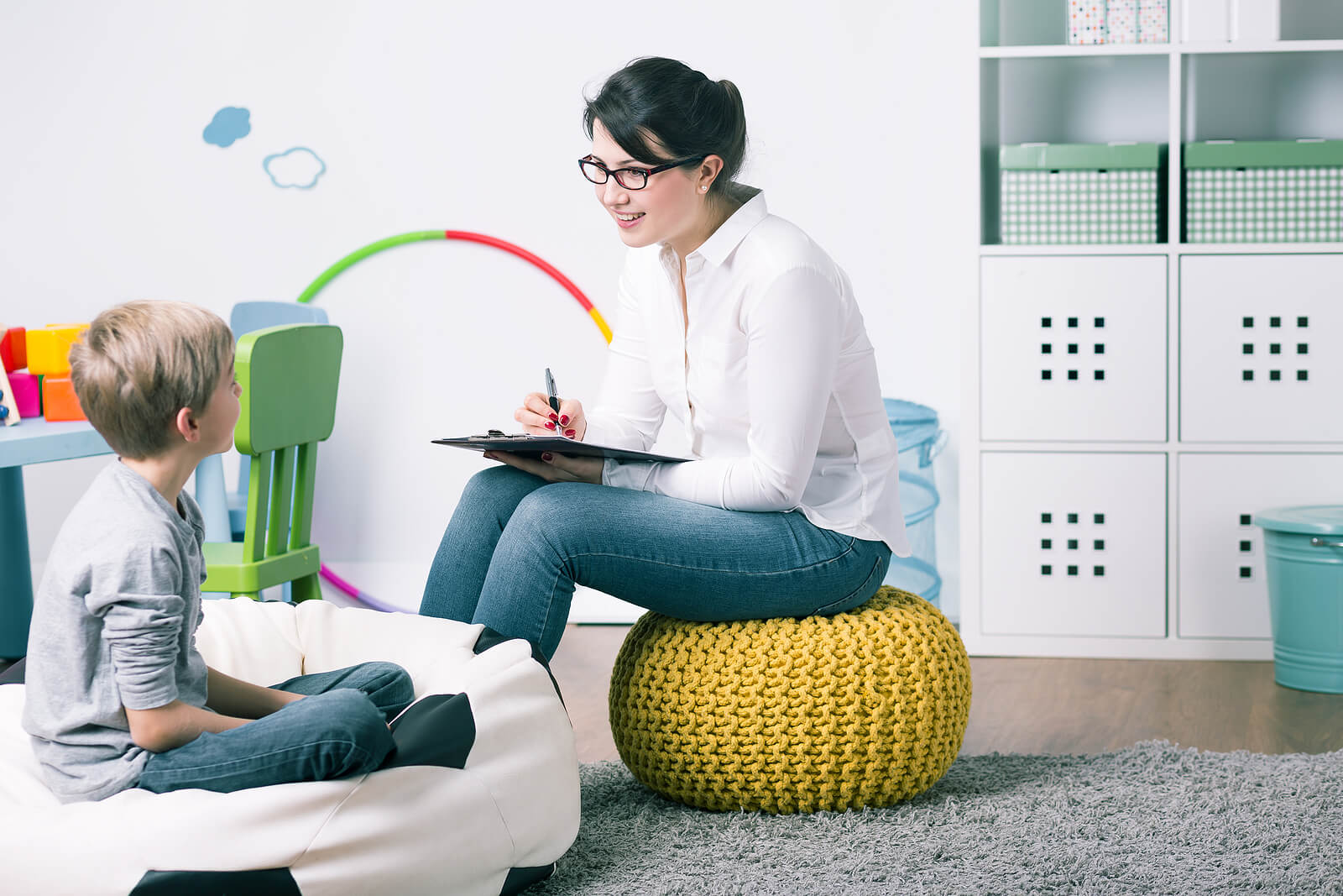 Smiling female therapist sitting on a cushion speaking to a little boy. With therapy for children in South Jersey your child can begin to thrive and heal from their anxiety, depression, and more in healthy ways.