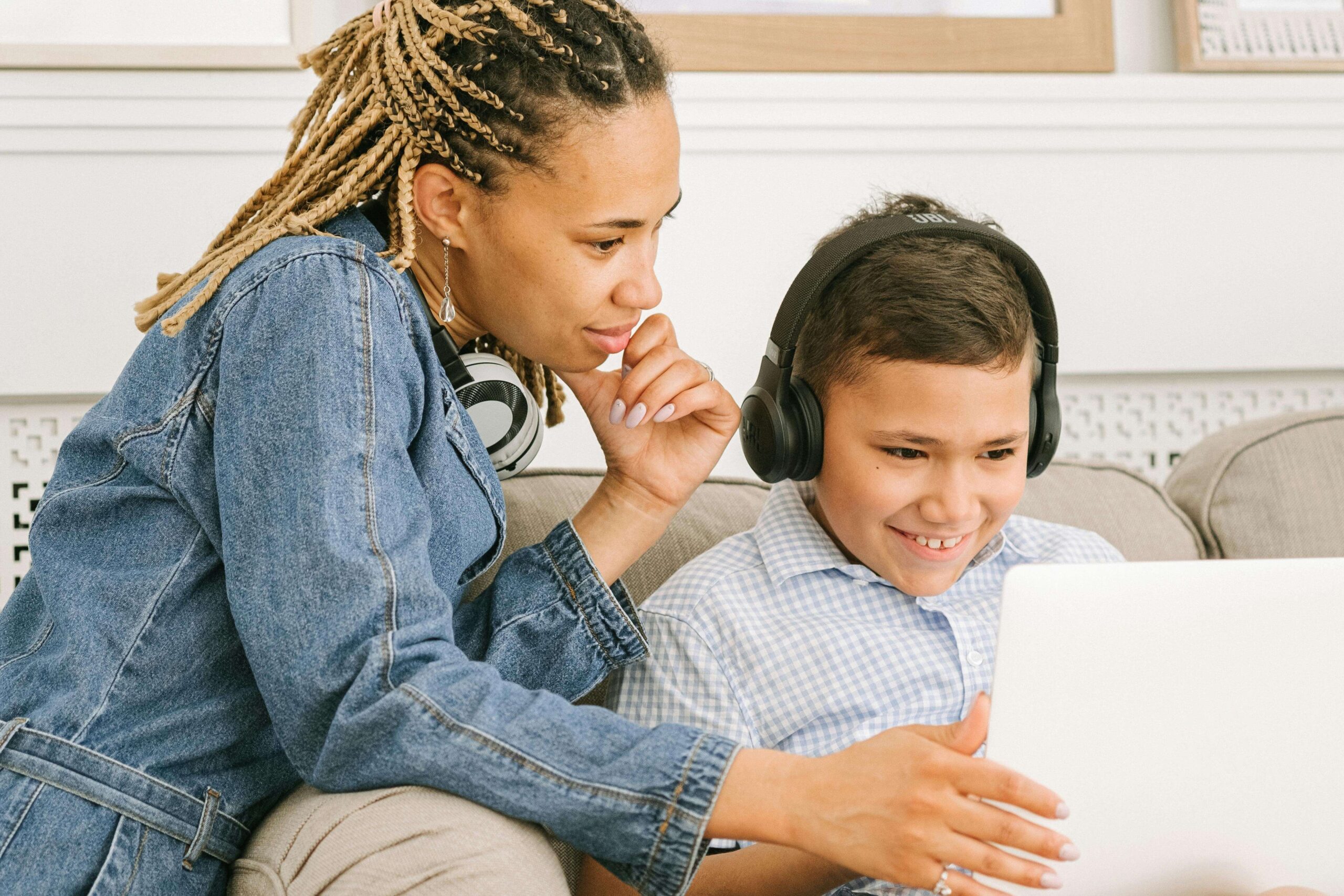 Smiling little boy, sitting next to a woman on a couch looking at a laptop. See positive changes in the way your child manages their emotions with the support of a supportive child therapist in South Jersey.