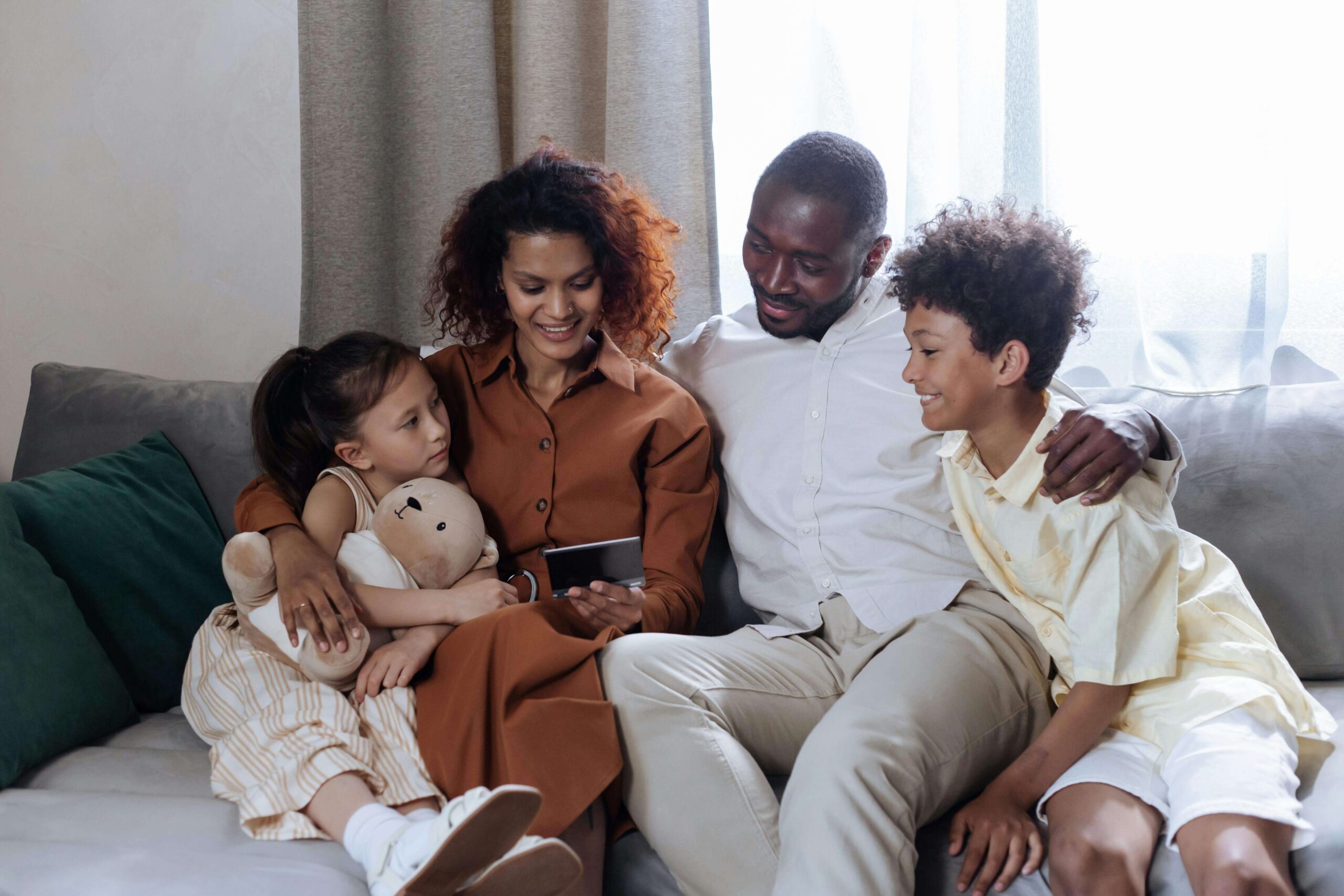 Happy family sitting on a couch hugging and looking at a cell phone. With therapy for children in South Jersey, your child can begin to overcome their overwhelming emotions in healthy ways to help them begin to heal.