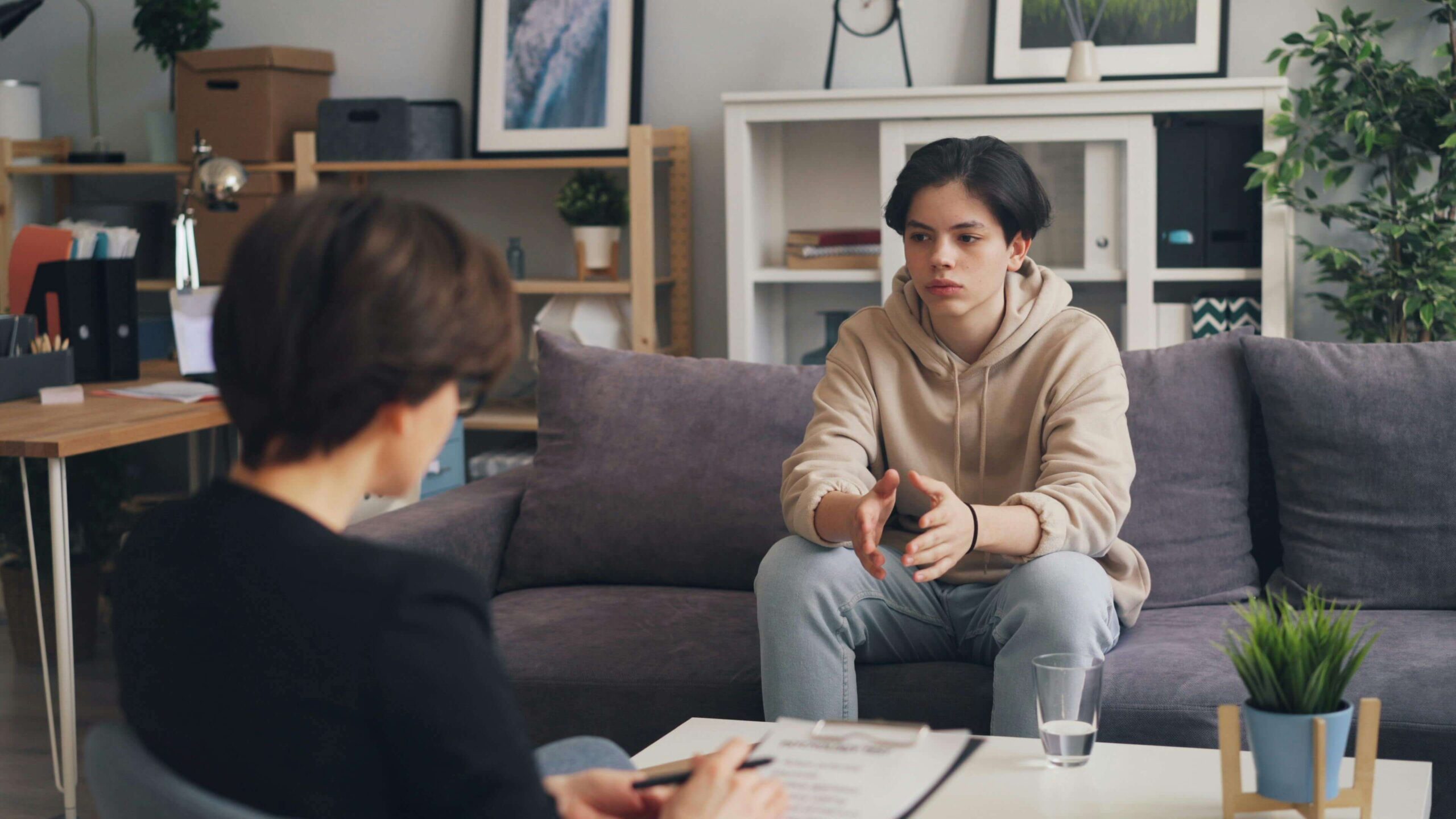 Teen boy in sitting on a couch speaking to a female therapist. Discover how therapy for children in South Jersey can help your child begin to manage their symptoms that relate to anxiety or trauma.