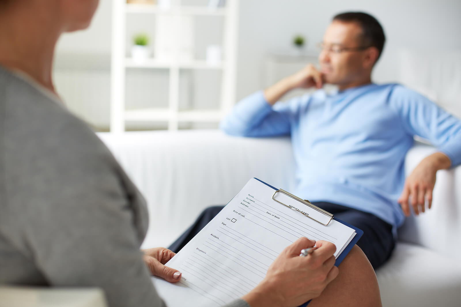 Man relaxing on a couch talking to a woman holding a clipboard. With neurodivergent therapy in South Jersey you can begin to cope with the challenges that come your way as a neurodivergent individual with support.