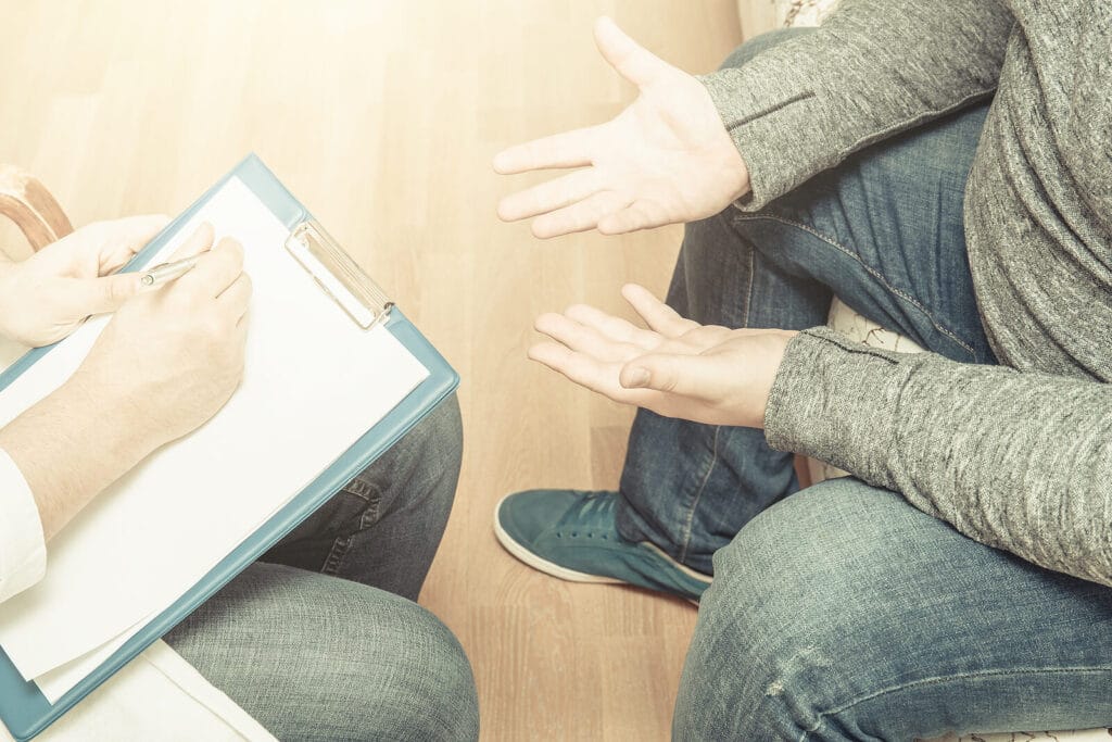 Man in therapy speaking to a therapist holding a clipboard. Begin to find clarity and confidence as a neurodivergent adult with ADHD testing in South Jersey.