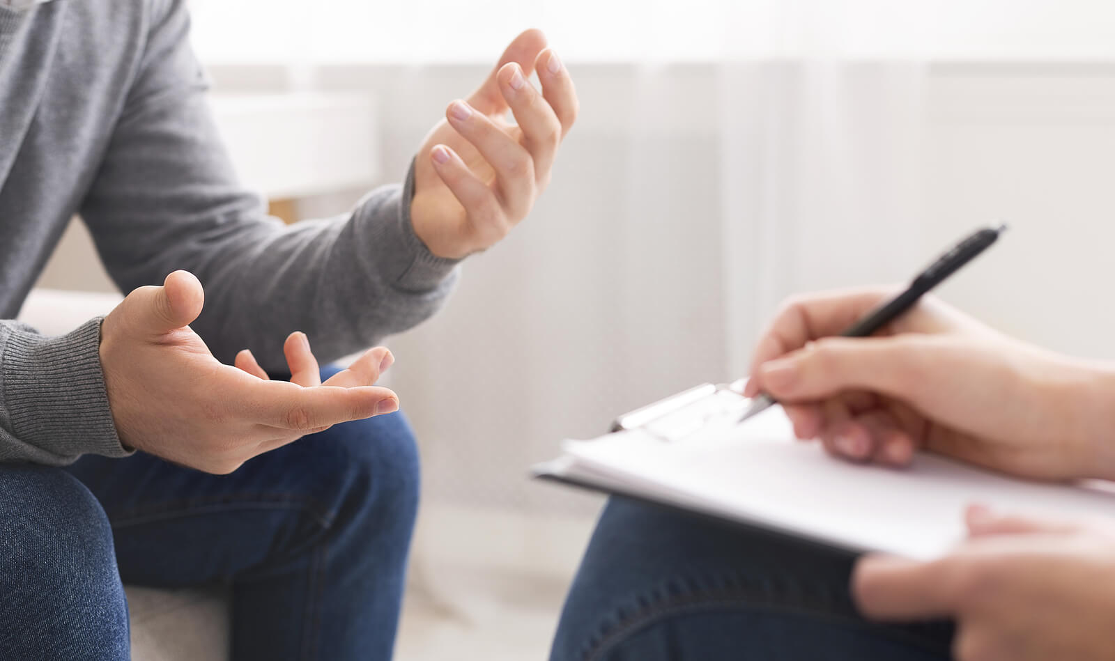 Man sitting on a couch gesturing with hands as a therapist sits across writing on a clipboard. Gain knowledge about ADHD or Autism and find support navigating your neurodivergent traits with ADHD/Autism testing in South Jersey.