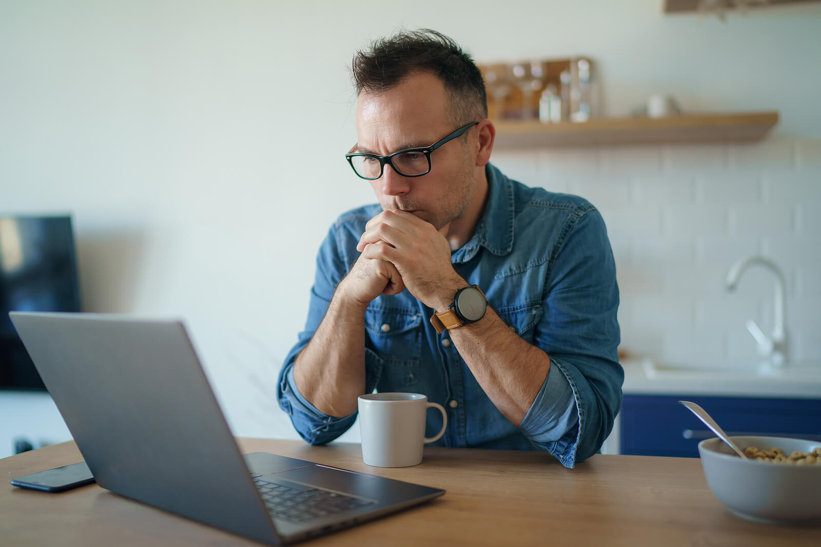 Thoughtful man sitting at a table looking at a laptop. With the support of a neurodivergent affirming therapist in South Jersey, you can navigate your unique needs as a neurodivergent individual.
