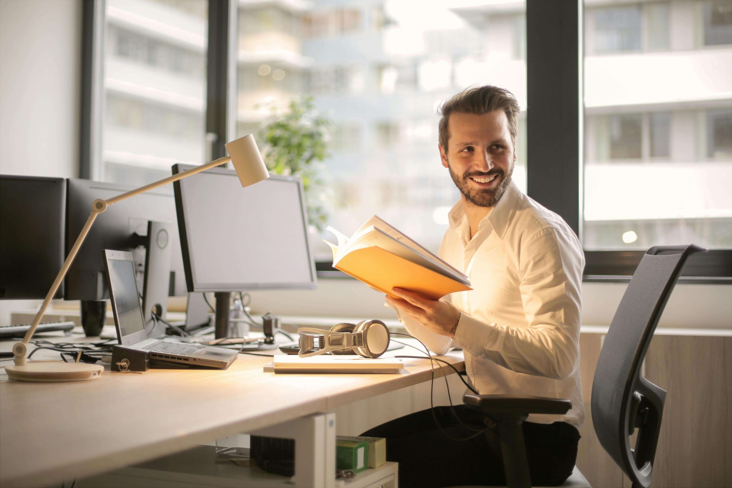 Happy professional man sitting at a desk holding a book. Embrace your unique strengths and build confidence with the help of affirming neurodivergent therapy in South Jersey.
