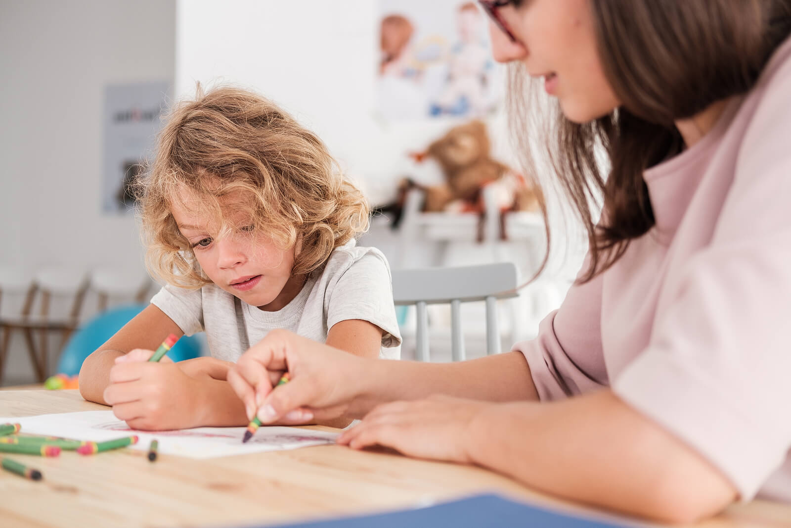 Young child coloring at a desk while a therapist guides with a crayon. With ADHD testing in South Jersey, families can find clarity early and support confidence through neurodivergent therapy.