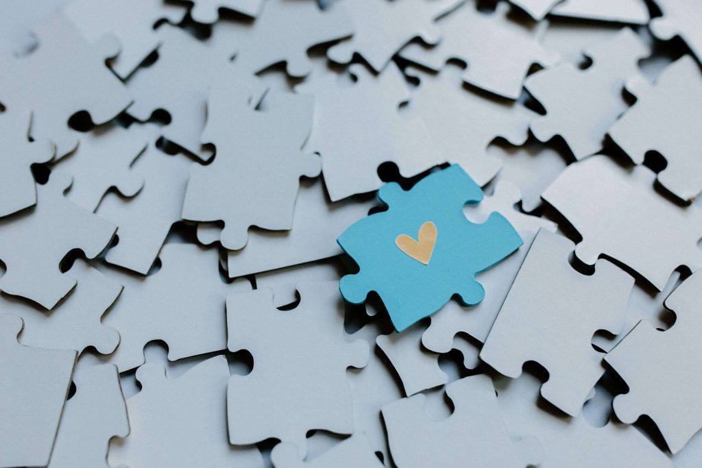 A single blue puzzle piece with a gold heart stands out among gray pieces. Autism testing in South Jersey can bring clarity and hope through autism assessment, helping both children and adults feel understood and supported.