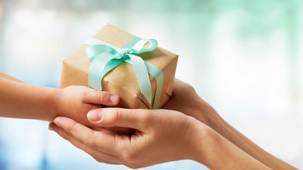 Hands giving gifts with blue bow. Handling financial stress over the holidays is possible with help from a skilled New Jersey therapist.