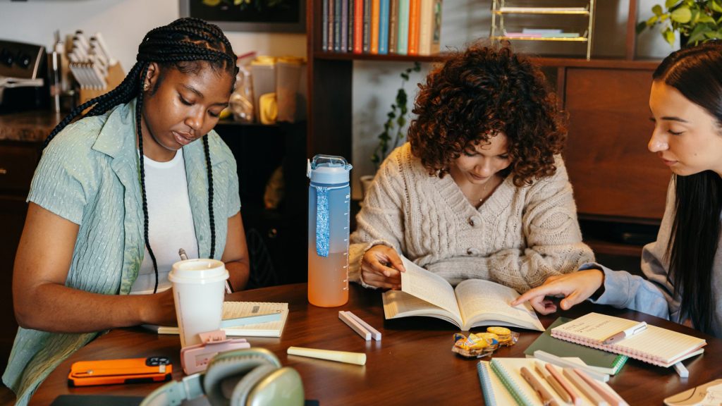 Two young women sit together at a cafe table with notebooks and coffee, studying and supporting each other, reflecting the kind of community support DBT of South Jersey offers in Voorhees and Moorestown, NJ