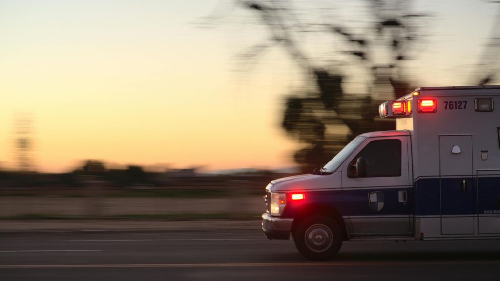 An ambulance with its emergency lights on speeds past at sunset, representing the demanding work of first responders who find DBT and trauma therapy support at DBT of South Jersey in Voorhees and Moorestown, NJ
