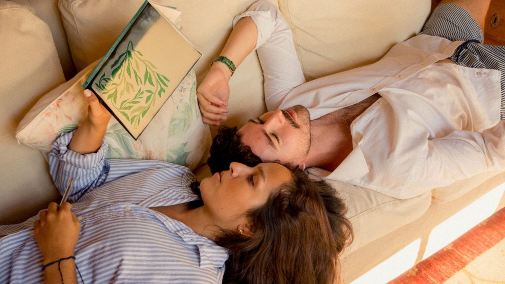 A couple relaxes together on a cream couch while one partner reads a book, showing the calm connection that DBT relationship skills help build for couples in Voorhees and Moorestown, NJ